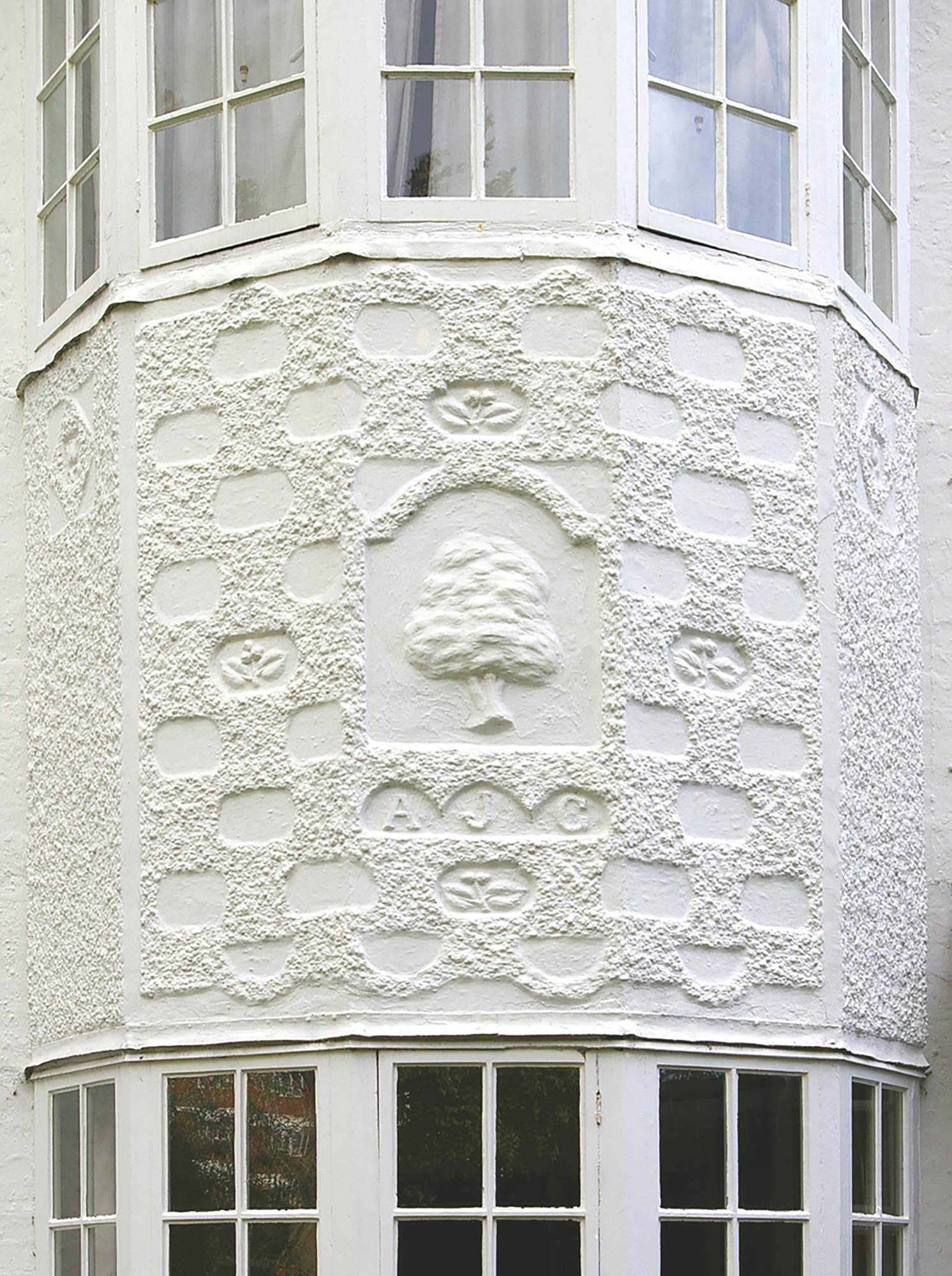 An ornate white bay window at The White House in Leicester, featuring textured plasterwork, floral details, and a central tree motif with the initials "A J C." - Leicestershire County Council, from the Leicester Evening Mail Photography Collection. Archived under "The White House, Scraptoft Lane," available via Image Leicestershire.